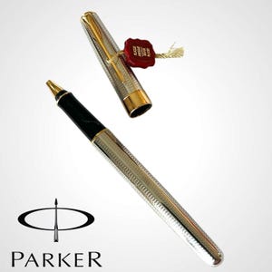 May include: A silver-plated Parker pen with a black grip and gold accents. The pen is partially disassembled, with the cap off, revealing the gold-colored nib. A red seal with gold text hangs from the cap. The Parker logo is visible.