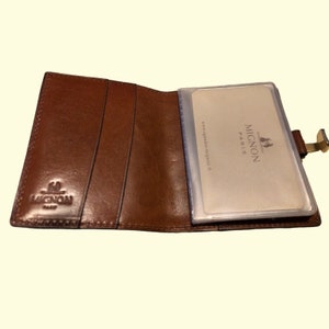 May include: Brown leather wallet with a clear plastic card holder. The card holder has the text "MIGNON PARIS" and "www.agenda-mignon.com".