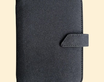 May include: A black fabric-covered planner with a flap closure and a stitched design.