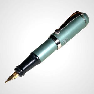 May include: A teal fountain pen with a gold nib and a black grip. The pen has silver accents on the clip and bands. The pen's body has a smooth, matte finish. A small logo is visible on the pen's body.