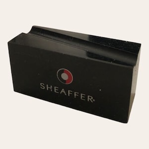 May include: Black rectangular pen stand with a silver SHEAFFER logo and a red and white circle logo.