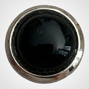 May include: A circular object featuring a polished silver-toned metallic rim surrounding a smooth, deep black center. The surface of the black insert is glossy and reflective, creating a high-contrast appearance against the metallic border.