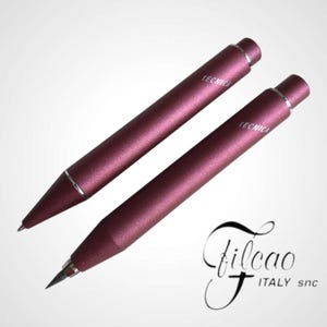 May include: Two burgundy-colored mechanical pencils with the word "TECNICA" printed on the barrel. The pencils have silver accents and a sleek design. The image also includes the Filcao Italy logo.