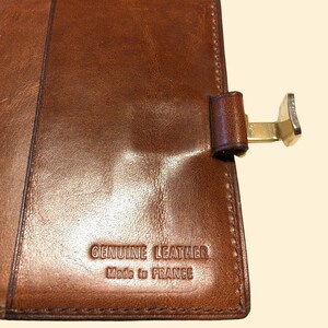 May include: A brown leather wallet with a gold metal clasp. The wallet has the text "GENUINE LEATHER Made in FRANCE" embossed on the front.