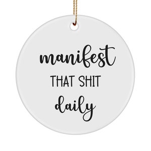 May include: White round ceramic ornament with black text that reads "manifest that shit daily".