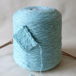May include: A skein of light blue yarn with a small knitted swatch, wooden knitting needles, and a label that reads "loopydot".