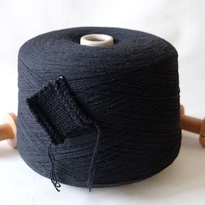 Peut inclure: Une pelote de fil noir enroulée sur une bobine en bois avec un petit échantillon de tricot noir attaché. Le fil est étiqueté "loopydot".