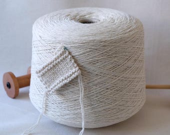 May include: A skein of natural white yarn wound on a spool. A small knitted swatch is attached to the yarn.