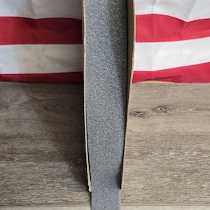 May include: A roll of gray, textured hook and loop tape, partially unrolled from a cardboard container. The background features an American flag and a wooden surface.