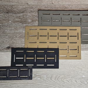 May include: Four rectangular panels in varying sizes and colors: dark gray, tan, black, and a smaller dark gray. Each panel has a series of evenly spaced, horizontal slots cut into the surface. The panels are arranged on a light wood-grain surface.