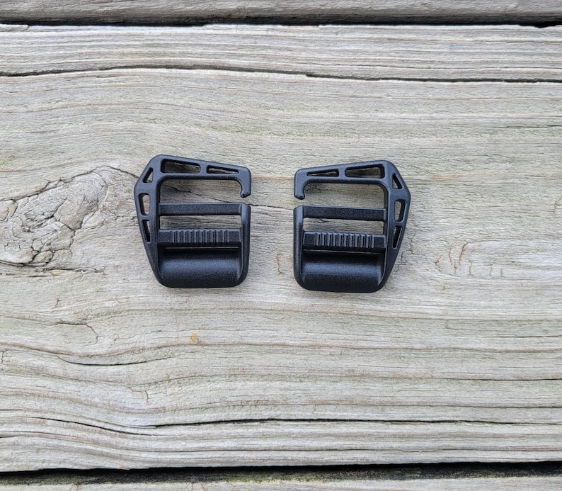 May include: Two black plastic buckle clips for straps or webbing. The clips have a rectangular shape with a small opening on one side and a locking mechanism on the other.