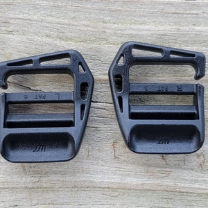 May include: Two black plastic buckles with a 'L PAT' and 'R PAT' marking on each. The buckles are designed for use with straps or webbing.