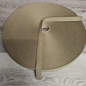 May include: A roll of tan nylon webbing, a type of heavy-duty fabric used for straps, belts, and other applications.