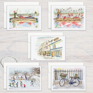 May include: A collection of watercolor greeting cards featuring various winter scenes. The cards depict people on a boat, a street with shops, ice skating, and a bicycle with a basket of flowers. Each card is paired with a white envelope.