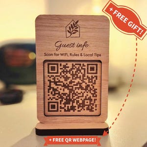 Könnte beinhalten: Hölzernes Gästeinformationsschild mit einem QR-Code. Das Schild zeigt "Guest info" und "Scan for WiFi, Rules & Local Tips". Ein rotes Banner zeigt "+ FREE GIFT!" und ein anderes "+ FREE QR WEBPAGE!"