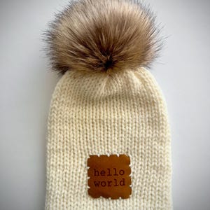 Touca de tricô artesanal de camada dupla para recém-nascido com pompom de pele sintética e aplique &quot;Hello World&quot; - Creme
