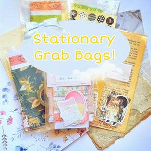May include: A collection of stationery grab bags featuring various paper goods, including patterned washi tape, stickers, and decorative sheets. The items are packaged in clear plastic sleeves, with a central overlay text reading Stationary Grab Bags!