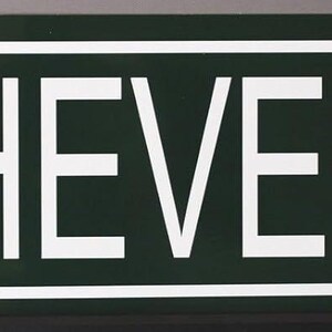 Peut inclure: Un panneau de rue rectangulaire aux coins arrondis. Le panneau est vert foncé avec le texte blanc "66 CHEVELLE DR.". Les chiffres et les lettres sont en gras, en police sans empattement, et le panneau a une bordure blanche.