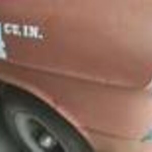 May include: Close-up of a vintage brown car's front quarter panel. White text reads "454 cu. in." on the side. The car has a chrome headlight and a black tire with a white rim. The paint shows signs of age.