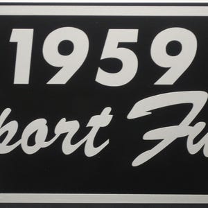 May include: Black and silver metal license plate with the text "1959 Sport Fury" in white.