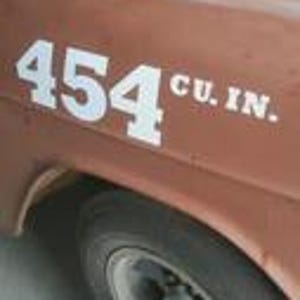 May include: Close-up of a weathered, brown vehicle's side. Bold, white text reads "454 CU. IN." near the front wheel. The image highlights the vehicle's vintage aesthetic and engine displacement.