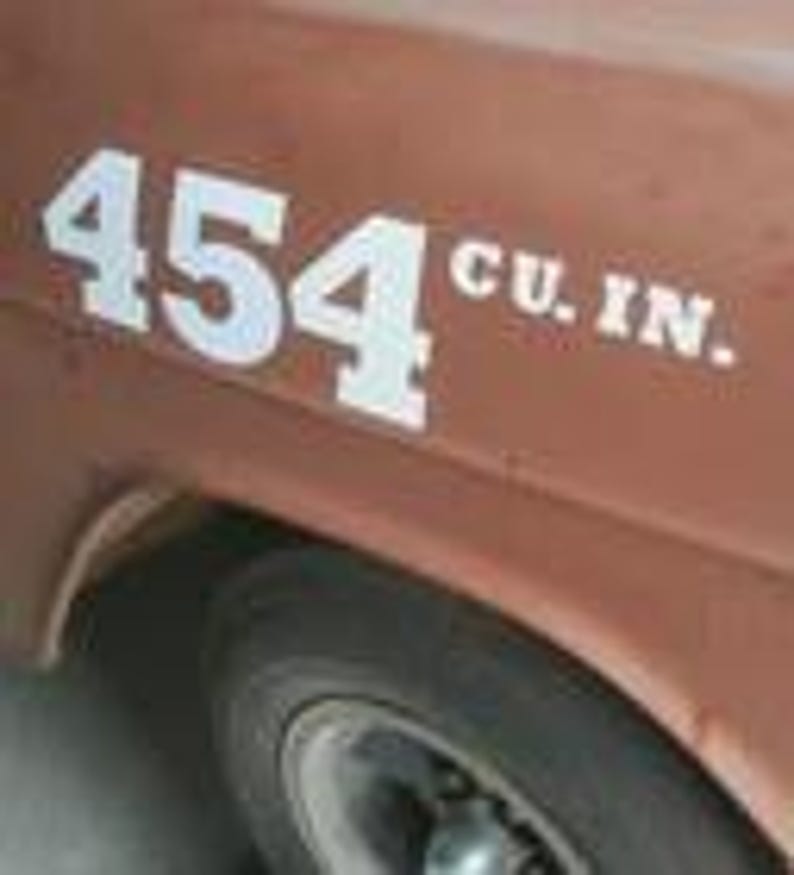 May include: Close-up of a weathered, brown vehicle's side. Bold, white text reads "454 CU. IN." near the front wheel. The image highlights the vehicle's vintage aesthetic and engine displacement.