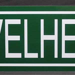 Puede incluir: Un letrero de calle rectangular verde con letras blancas que dice "SHOVELHEAD DR.". El letrero tiene un borde blanco y está montado sobre una superficie oscura. El texto está en negrita, fuente sans-serif.