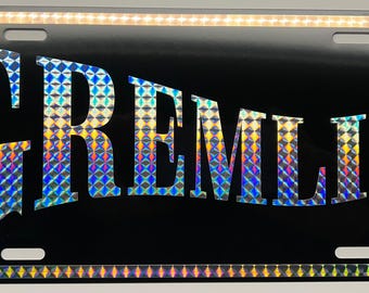 Placa metálica GREMLIN de 12 x 6 pulgadas, negra, con letras PRISM retro de los 70 y la inscripción AMC.