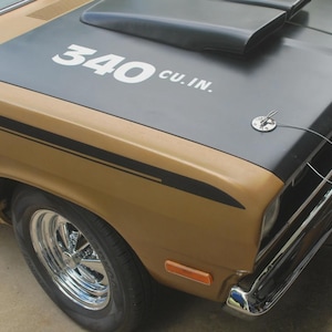 May include: Close-up of a classic gold and black muscle car. The hood features the text "340 cu. in." in white. The car has chrome accents and a black hood scoop.