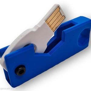 Może przedstawiać: Niebiesko-biały uchwyt na pendrive. Uchwyt jest niebieski z białą wkładką, która trzyma pendrive. Pendrive jest widoczny i ma złoty konektor. Czarna śruba jest widoczna z boku niebieskiego uchwytu.