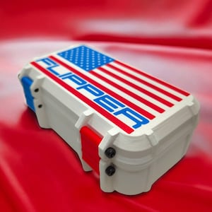 May include: A white plastic case with a red, white, and blue American flag design and the word "FLIPPER" printed in blue letters. The case has a blue latch and red hinges.