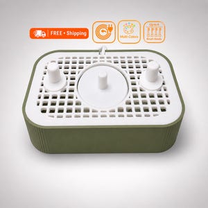 May include: An olive green rectangular electric toothbrush charging base with a white top surface featuring a grid pattern, three white vertical pegs for brush heads, and icons indicating multi-colour options and capacity for up to 4 brush heads.