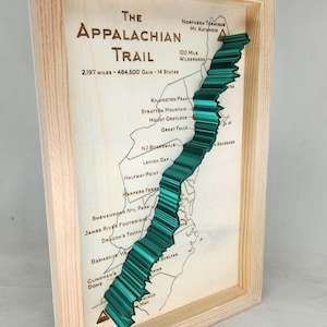 Peut inclure: Carte encadrée en bois du sentier des Appalaches. La carte présente une représentation verte en trois dimensions du tracé du sentier. Le texte sur la carte comprend "The Appalachian Trail" et les statistiques du sentier.
