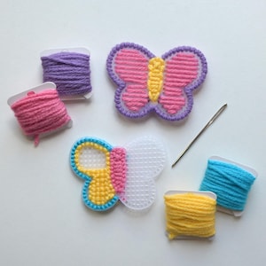 May include: A craft kit with two butterfly shapes, one with pink and yellow yarn and the other with a white plastic canvas. The kit includes four spools of yarn in purple, pink, yellow, and blue.
