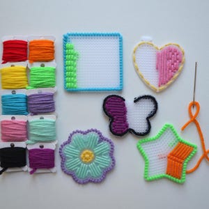 May include: A set of colorful plastic canvas embroidery kits with various shapes including a heart, butterfly, flower, and star. The kits include floss in a variety of colors and a needle.