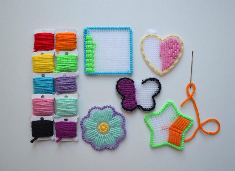 May include: A set of colorful plastic canvas embroidery kits with various shapes including a heart, butterfly, flower, and star. The kits include floss in a variety of colors and a needle.