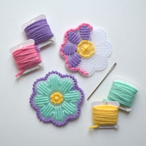 May include: Five spools of embroidery floss in pink, purple, yellow, green, and light blue, with two plastic canvas flowers with a yellow center, one with purple and pink embroidery and the other with light blue and purple embroidery.