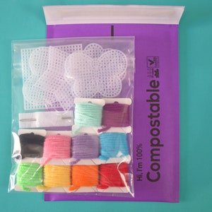 May include: A set of colorful embroidery floss and white plastic canvas shapes in a clear plastic bag. The bag is labeled "Hi, I'm 100% Compostable" with a green leaf logo.