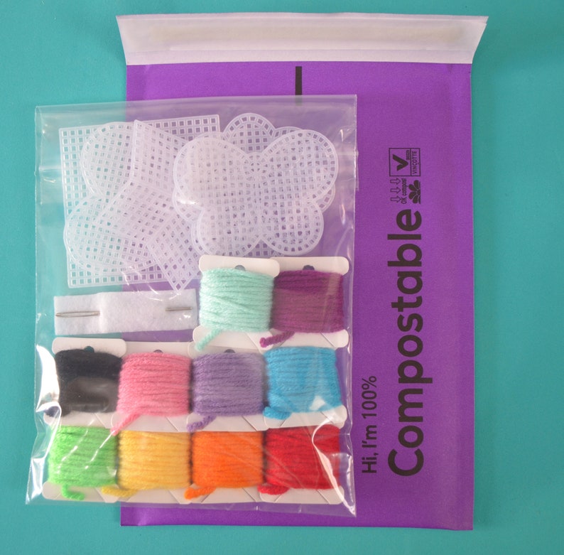 May include: A set of colorful embroidery floss and white plastic canvas shapes in a clear plastic bag. The bag is labeled "Hi, I'm 100% Compostable" with a green leaf logo.