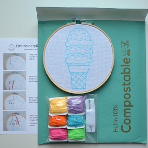 May include: A DIY embroidery kit with a white embroidery hoop featuring a blue ice cream cone design. The kit includes four spools of colourful embroidery floss, a needle, and a piece of white fabric. The packaging is green and says "Hi, I'm 100% Compostable".