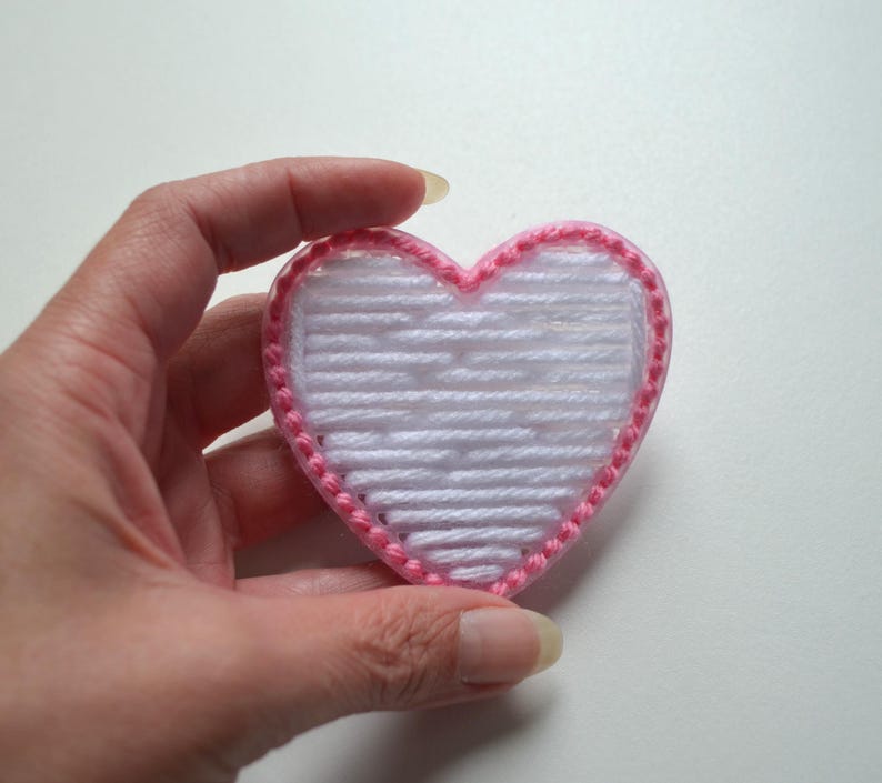 May include: A white heart-shaped yarn craft with a pink yarn border.