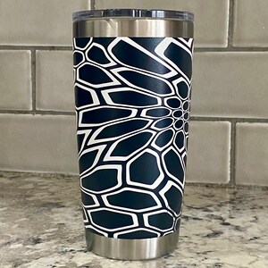 May include: A stainless steel tumbler with a black and white geometric pattern. The pattern resembles a flower with a circular center.