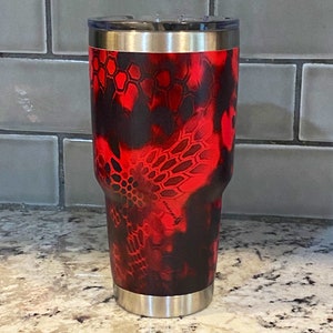 May include: A stainless steel tumbler with a red and black camouflage pattern. The tumbler has a double-walled design and a lid.