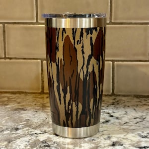 May include: A stainless steel tumbler with a camouflage pattern. The tumbler has a lid and is designed for hot or cold beverages.