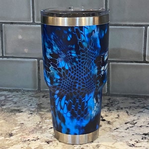 May include: A blue and black patterned stainless steel tumbler with a lid. The pattern resembles a camouflage design.
