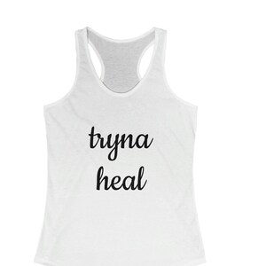 May include: White tank top with the text "tryna heal" printed in black.