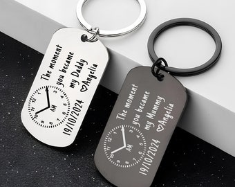 May include: Two silver and black keychains with a clock face and the text "The moment you became my Daddy/Mummy 19/10/2024 Angelia".