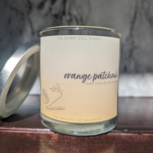 Puede incluir: Un tarro de vidrio para velas con una etiqueta blanca que dice "THE SUNNY SOUL STUDIO" y "orange patchouli sweet citrus & rich incense". La etiqueta también dice "SOY WAX 9 FL OZ/255 GRAMS".