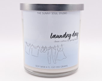 Peut inclure: Un bocal de bougie blanc avec un couvercle argenté. L'étiquette indique "THE SUNNY SOUL STUDIO Laundry day clean cotton & spring breeze SOY WAX 9 FL OZ/255 GRAMS". L'étiquette présente également une ligne de vêtements suspendus à une corde à linge.