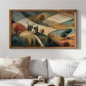 May include: A framed landscape painting depicts rolling hills in shades of brown, green, and blue. A small white house sits on a hill with a winding path leading to it. The artwork is in a wooden frame and hangs above a white sofa.
